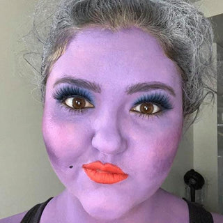 Nia Hames wearing purple face paint, styled grey hair, blue eyeshadow, bold lashes, and colored contacts.