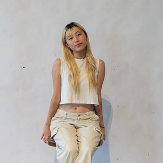 Joohyeon Park with blonde hair sits on a stool wearing a white crop top and beige cargo pants.