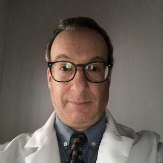 David Jupiter wearing round black glasses, a blue collared shirt, tie, and white lab coat.