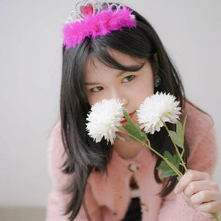 Olivia Pauline wearing a pink feathered tiara and holding white flowers.