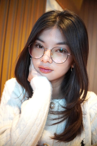 Amaya Chin with dark eyes wearing thin round metal glasses and resting her chin on her hand.