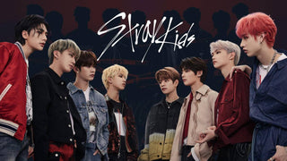Eight members of K-pop group Stray Kids pose together against a dark backdrop beneath the white Stray Kids logo.