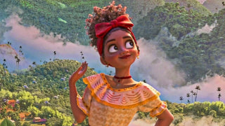 Dolores from Encanto wearing a yellow ruffled blouse and red bow headband against lush green mountains.