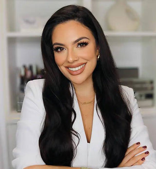Monica Jacome smiling in a white blazer with long dark hair, false lashes, and burgundy nails.