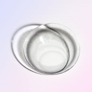 Macro shot of a black eye contact lens (or a circle lens), showing a thin black limbal ring that gives an eye-enlarging effect, on a light background.