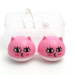 Two round, pink, cat-like objects with cartoon faces, black eyes, and small ears, placed in front of a clear plastic container. The faces have blush marks and small puckered mouths.