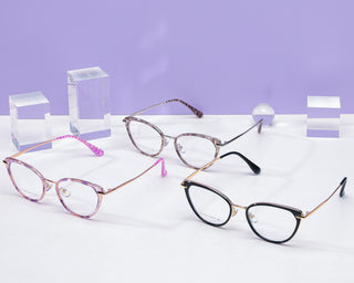 Various colors (purple, purple tortoiseshell and black) of the Aura cat-eye vintage eyeglass frame, available in blue light blocking lenses and readers, photographed on a purple background, from EyeCandys