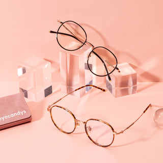Banger round vintage prescription eyeglasses, pictured in tortoiseshell and black/gold, available in blue light blocking lenses and in readers with magnification, from EyeCandys, photographed on a pink background