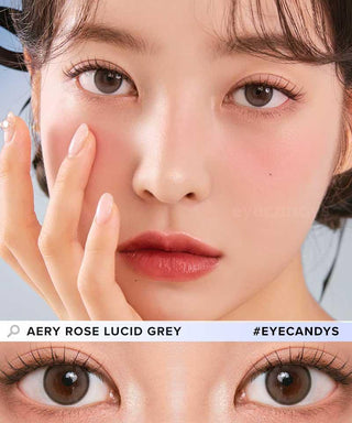 Beautiful female Asian model wearing Eyecandys Aery Rose Lucid Grey contact lenses and natural makeup. The model's hand is on her face, emphasizing the attractiveness of her eyes using the contact lens. The image shows her dark brown eyes using grey tone contact lenses with a natural appearance.