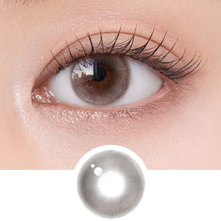 Close-up shot of model's eye adorned with Chuu Aube Pie Moon Beige (10pk) daily color contact lenses with prescription, complemented by clean eye makeup, showing the brightening and enlarging effect of the circle contact lens on dark brown eyes, above a cutout of the contact lens pattern with limbal ring on a white background.