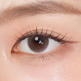 Close-up shot of model's eye adorned with Chuu Aube Pie Moon Brown (10pk) color contact lenses with prescription, complemented by minimalist eye makeup, showing the brightening and enlarging effect of the circle contact lens on dark brown eyes.