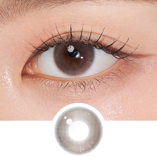 Close-up shot of model's eye adorned with Chuu Aube Pie Moon Brown (10pk) daily color contact lenses with prescription, complemented by clean eye makeup, showing the brightening and enlarging effect of the circle contact lens on dark brown eyes, above a cutout of the contact lens pattern with limbal ring on a white background.