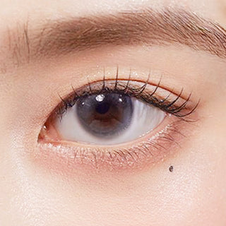 Close-up shot of model's eye adorned with Chuu Aube Pie Moon Grey (10pk) color contact lenses with prescription, complemented by minimalist eye makeup, showing the brightening and enlarging effect of the circle contact lens on dark brown eyes.