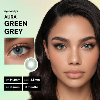 A woman with long dark hair wears EyeCandys Aura Green Grey contacts in close-up. These UV-blocking lenses create a jewel-toned eye effect. Specs: DIA 14.2mm, G.DIA 13.6mm, B.C. 8.7mm, usable for 3 months. "EyeCandys Aura Green Grey" appears onscreen.