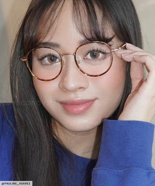 Female model wearing the Sunlit Hazel enlarging prescription circle lenses under a pair of tortoiseshell round eyeglasses