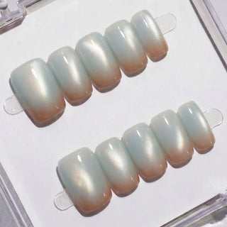 Two sets of EyeCandys Blue Hour Latte Press-On Nails with a glossy, pearlescent finish fade from soft white tips to natural beige bases—displayed on white, perfect for a salon-quality gel manicure look at home.