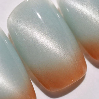 Close-up of EyeCandys Blue Hour Latte Press-On Nails—three handmade nails feature a smooth, glossy gradient from shimmery light blue tips to warm peach bases, perfectly mimicking a salon-quality gel manicure.