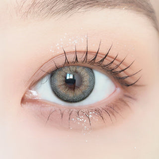 Close-up of model's eye wearing with Ann365 Buttercup Grey Korean color contact lens with prescription, complemented with barely there eye makeup, showing the brightening and enlarging effect of the circle lens on dark brown eyes.