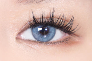 Close-up of natural dark brown eye with wispy lashes wearing EyeCandys Doe Blue colored prescription contact lens for a soft, natural look