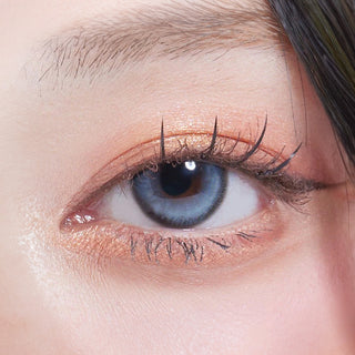 Close-up shot of model's eye adorned with Eyesm Dollring Chole Blue prescription colored contacts, complemented by clean eye makeup, showing the brightening effect of the prescription cosmetic contact lens on dark brown eyes.
