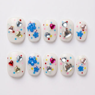 Dot Cake Press-On Nails by EyeCandys: reusable white gel nails with colorful round dots, blue flower designs, and shiny heart and round rhinestones—handmade and neatly arranged in two rows on a white background.