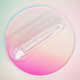 A round, semi-transparent coaster with a pink-to-white gradient sets the background. On top rests a white hair clip bearing the word "CANDY," positioned diagonally. Nearby, tweezers from the EyeCandys Contact Lens Case Applicator Kit add a charming detail to the scene, while soft lighting enhances the gentle, pastel effect.