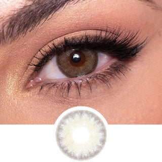 Close-up image of a person's eye with a brown iris and black eyeliner. The person is wearing long, voluminous eyelashes. Below the eye, there is an image of a light brown colored contact lens, suggesting that the person might be wearing EyeCandys Isla Set (3 Pairs) by EyeCandys shown.