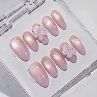 EyeCandys Lilac Dew Press-On Nails: A glossy, light pink set in a clear case. Two nails have 3D white and pink flowers; others feature subtle magnetic shimmer with small raised dots for extra detail.