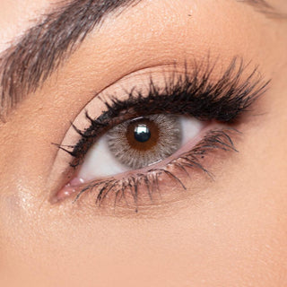 Close-up shot of a model eye wearing multi-tone grey (Pink Label Los Angeles) colored contact lens in one eye that is naturally dark-brown with natural eye make up