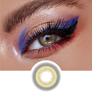 A green/hazel contact lens on top of a brown eye with blue artistic eye makeup and long eyelashes, above the design of the contact lens itself.