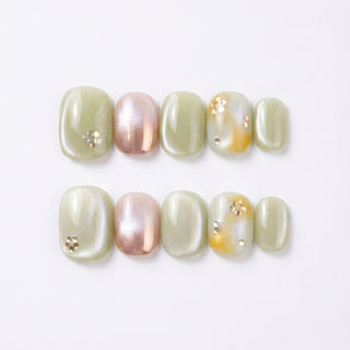 EyeCandys Matcha Made Press-On Nails: two handmade sets in pastel green and shimmery pink, some with metallic and white floral studs. Enjoy a flawless salon gel manicure look at home, arranged elegantly on a white background.