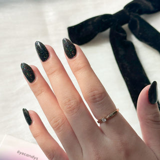 Hand with EyeCandys Meow Me Back Gel nail stickers applied, featuring a sleek black color with glitter accents. Perfect for edgy, glamorous manicures, offering long-lasting wear, easy application, and a sparkling, salon-quality gel finish for eye-catching nails.