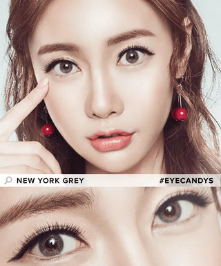 An Asian model with brown hair displaying New York Grey contact lenses on her naturally dark eyes, gently touching the corner of her eyes, with a close-up view emphasizing the lenses' impact.