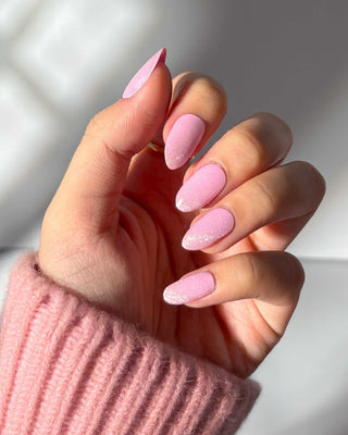 Hand showcasing EyeCandys Pilates Princess Gel Nail Stickers in sparkling pink with glitter. Easy-to-apply spring nails that last 2-3 weeks, featuring a 7-free, allergy-friendly formula. Cures in sunlight, no UV lamp required, for a chic and durable glittery nail design.
