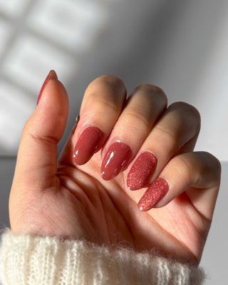 Hand featuring EyeCandys Strawberry Spice Gel Nail Stickers in a bright strawberry hue with glitter. Effortless spring nails that last 2-3 weeks, made with a 7-free, allergy-friendly formula. Cures in sunlight in 5-10 minutes, perfect for a fun and sparkling nail design.