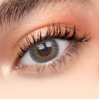 Close up of model wearing Pink Label New York Grey contact lenses on top of dark brown irises with natural curled lashes and peach eyeshadow