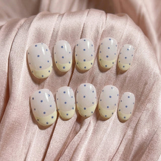 Sunday Dots press on nails by EyeCandys featuring off-white base, pastel yellow French tips, and periwinkle polka dots for a cute, wearable pastel manicure.