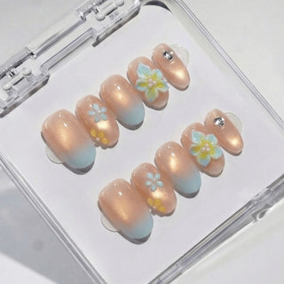 Almond press on nails Leiโd Back with soft nude base, golden shimmer gradient, baby blue tips, and sculpted 3D plumeria flower nail art.