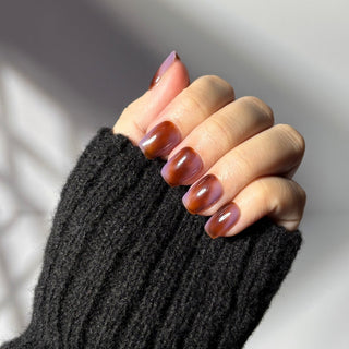 Hand showcasing EyeCandys Night Plum marbled press on nails in deep plum and auburn shades.