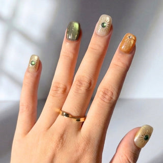 Hand wearing EyeCandys Sun Spell press on nails featuring a cat-eye design in nude, amber, and green with sun-inspired details.