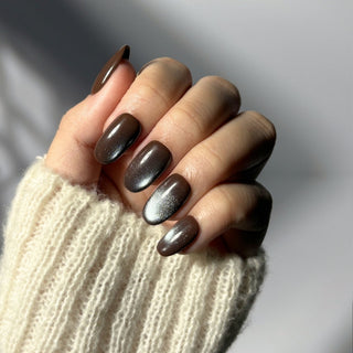 Hand showcasing EyeCandys Midnight Cocoa press on nails with rich dark brown base and shifting blue-grey cat-eye shimmer.