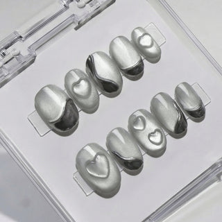 Close-up of EyeCandys Soft Signals press on nails featuring smooth grey cat-eye base with magnetic shimmer, silver chrome curves, and subtle sculpted heart accents on a white background.