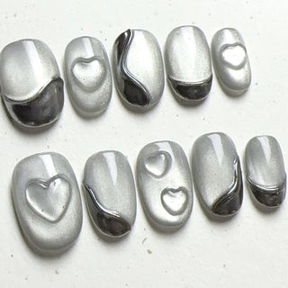 Close-up of EyeCandys Soft Signals press on nails on a white background featuring grey cat-eye base with subtle magnetic glow, silver chrome accents, and sculpted heart details.