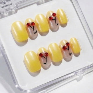 Close-up of EyeCandys Cherry Picnic press on nails featuring pastel yellow chrome finish with French tips and playful sculpted cherry details on a white background.