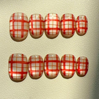 EyeCandys’ Picnic Date Press-On Nails feature a handmade red and white plaid design, arranged in two rows on a textured, light surface for an easy salon-quality gel manicure at home.