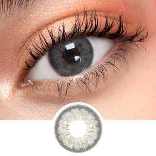 Close up shot of a model with natural dark eyes wearing EyeCandys Pink Label Angel Grey colored contact lens complemented by natural eye make up next to a cutout of the lens design