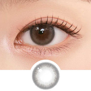 Close-up shot of model's eye adorned with Chuu Pompon Pop Bubble Grey (10pk)daily color contact lenses with prescription, complemented by natural eye makeup, showing the brightening and enlarging effect of the circle contact lens on dark brown eyes, above a cutout of the contact lens pattern with limbal ring on a white background.