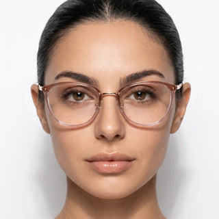 A woman with slicked-back dark hair and groomed brows looks at the camera, modeling EyeCandys Posh Square unisex glasses. The clear, full-frame style complements her smooth skin and neutral makeup against a plain white background.