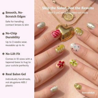 A close-up of hands with colorful, floral Pucker Up Press-On Nails by EyeCandys holding a gold heart locket. Features: smooth edges, no-chip durability, no-lift fit, and real salon gel manicure.