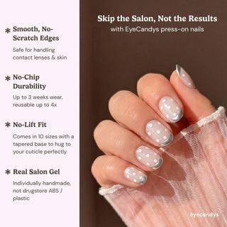 A hand displays EyeCandys Silver Spotted Press-On Nails—pale pink base, white polka dots, and metallic silver tips. Enjoy a no-chip, no-lift fit with the look of a real salon gel manicure.